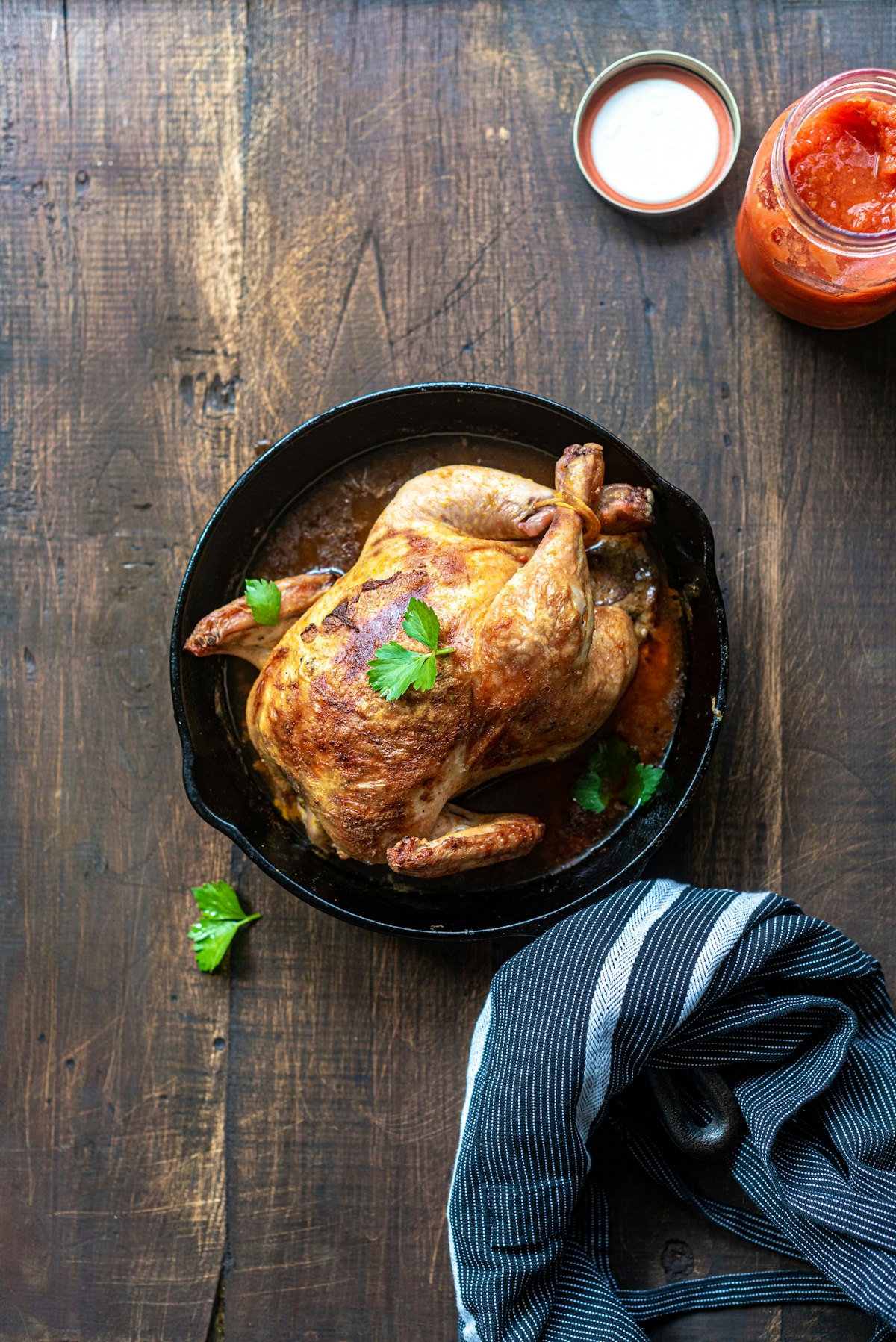 A whole roast chicken resting in a cast-iron skillet on a dark wood table