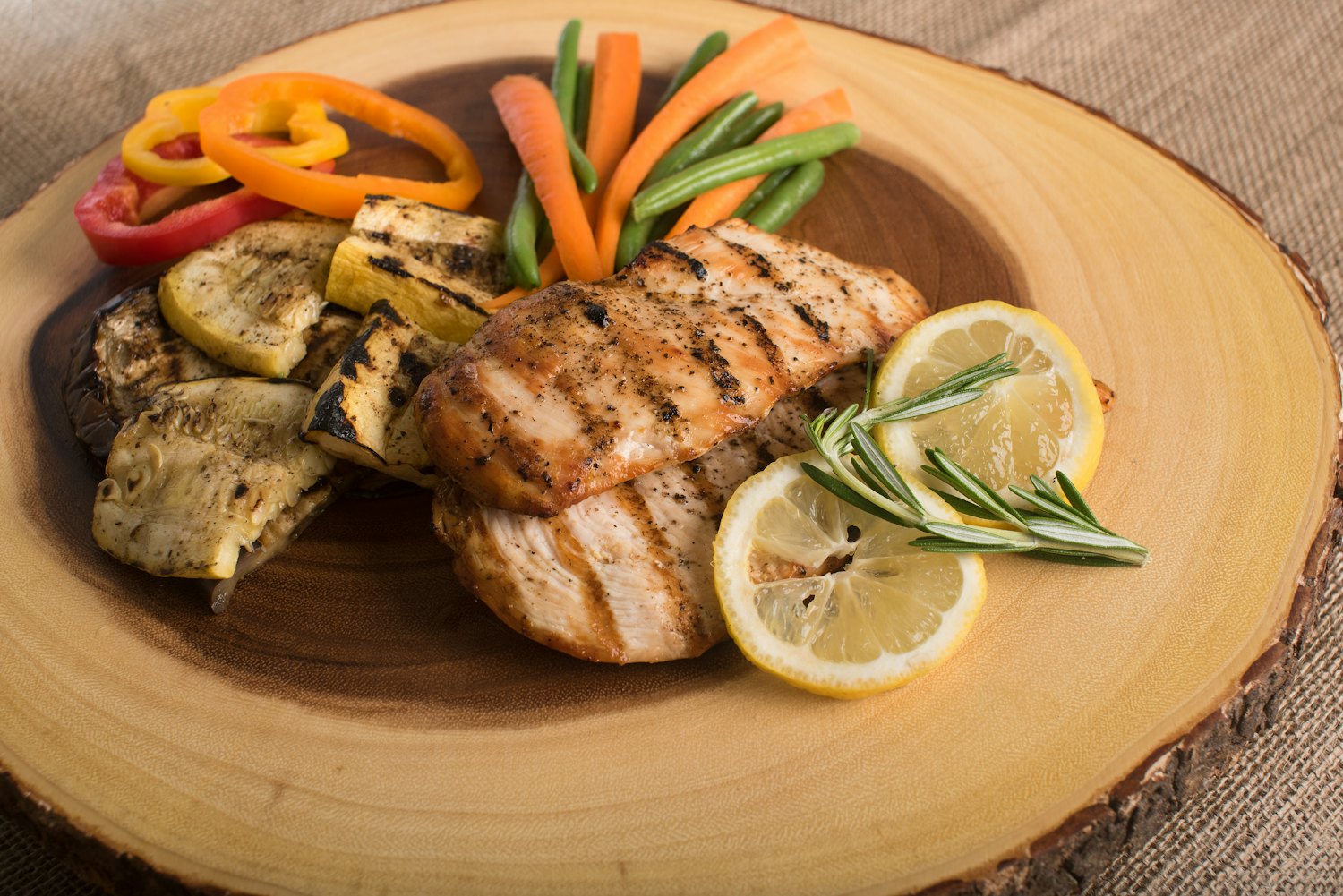 Grilled chicken breast with charred zucchini, peppers, green beans and lemon on a wooden board